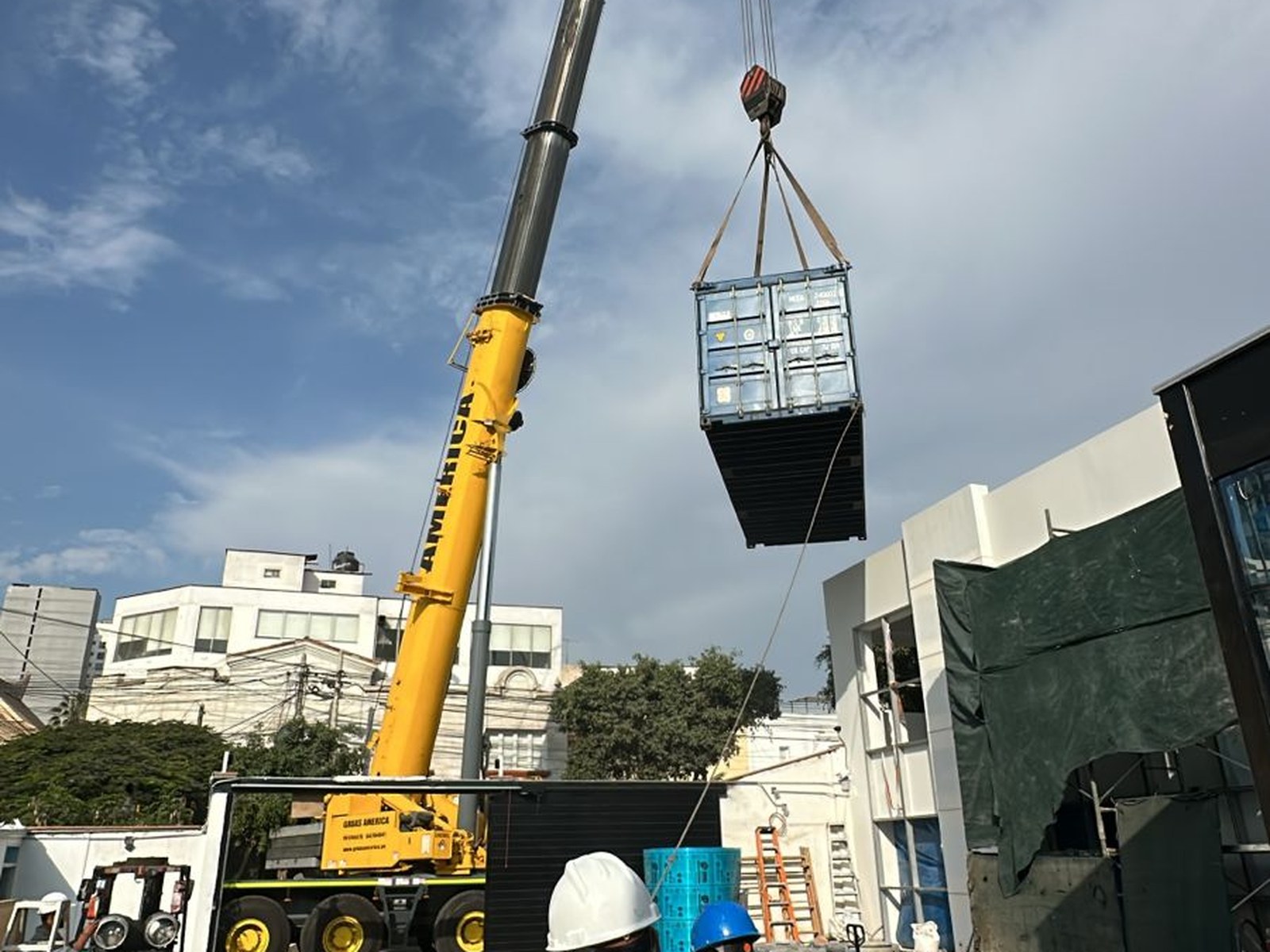 Izaje de un componente del equipo con una grúa de 30 toneladas hacia el interior del predio. Al fondo, el edificio en fase final de obra. La operación se ejecutó con el estacionamiento interior habilitado como zona de acopio y maniobra.