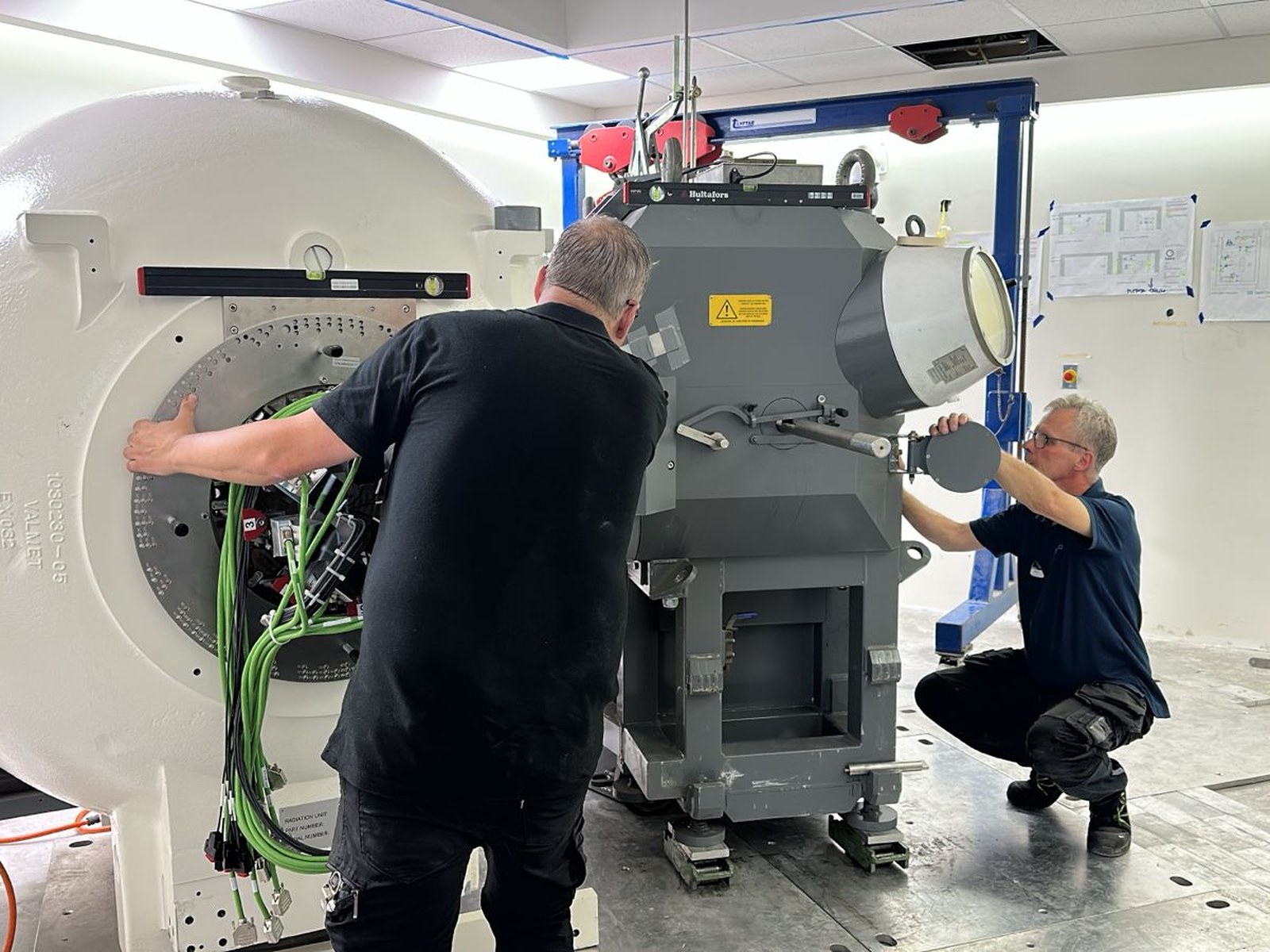 Técnicos de Elekta conectando la unidad de radiación al robot de instalación dentro del búnker. El cableado de fibra verde corresponde al sistema de control de posicionamiento del equipo durante la instalación de las fuentes radiactivas.