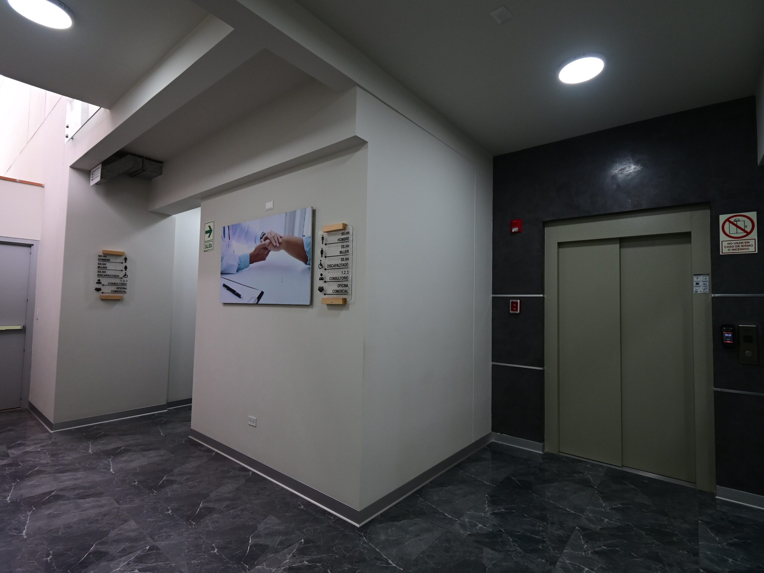 Hall de distribución con ascensor hacia el segundo piso. La circulación vertical, ausente en la sede anterior del IGKP, fue un requerimiento programático no negociable: el perfil del paciente —frecuentemente con compromiso neurológico o en silla de ruedas— exige accesibilidad vertical garantizada.